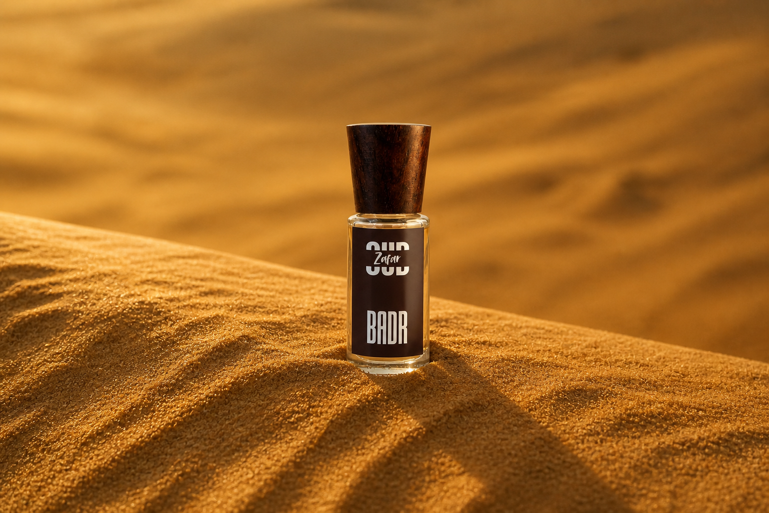 A single BADR Oud Zafar attar bottle standing naturally on a sunlit dune crest
